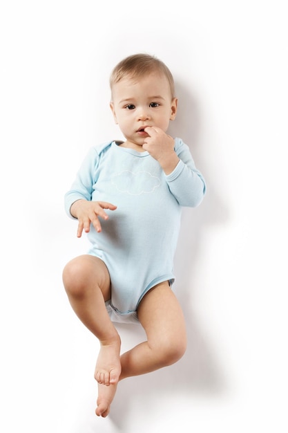 Little boy in romper lying on back and putting fingers in mouth