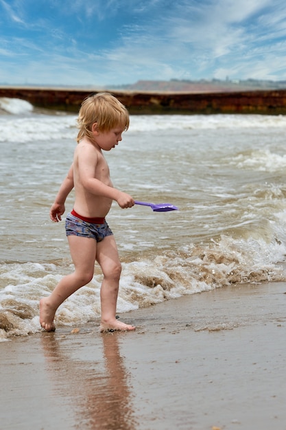 小さな男の子が海岸沿いの砂浜を走っています。海で休んでいる子供