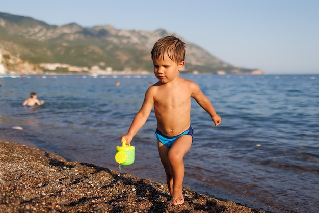 Little boy runs along the sandy shore with a toy sprinkler