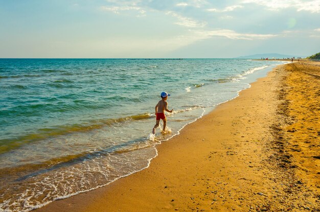 A little boy runs on the sand near the sea.