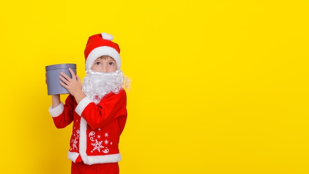 Ragazzino in abiti da babbo natale e con una barba artificiale che tiene in mano una scatola regalo rotonda