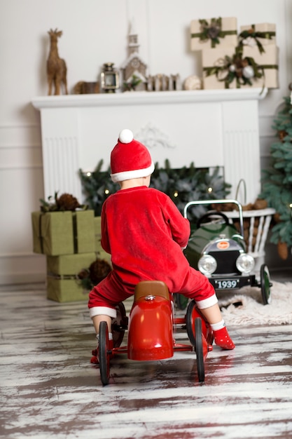 Foto il ragazzino in costume del babbo natale guida un'automobile di rosso del giocattolo