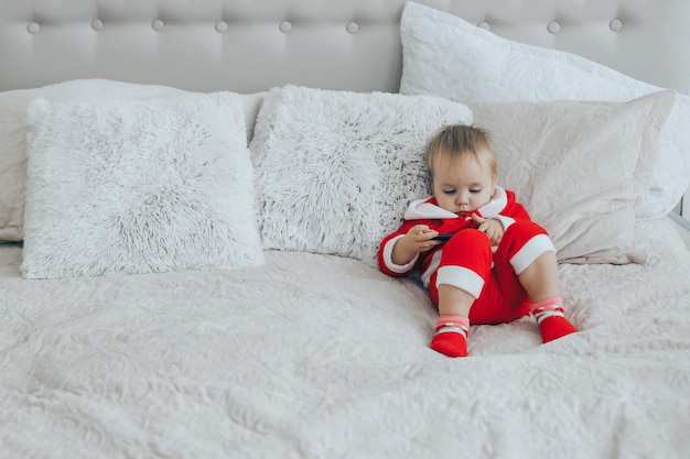 Little boy in Santa costume is playing with a mobile phone