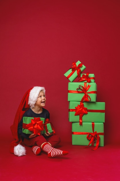 산타 모자를 쓴 어린 소년이 선물 상자 옆에 앉는다.
