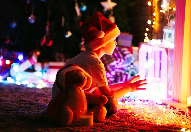 Little boy in Santa hat sitting at home on a Christmas surface