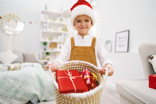 Little boy santa holding basket with decorated gifts for christmas