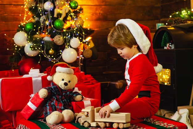 little boy in santa suit playing with his toys near the fireplace