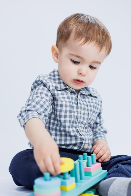 シャツを着た小さな男の子が白い背景にカラフルな木のおもちゃを作っている子供のおもちゃの子供の発達ゲームのコンセプト コピースペース