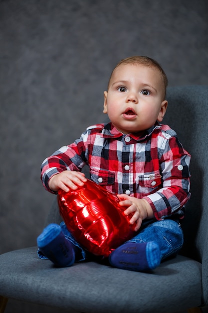 Маленький мальчик в рубашке играет с воздушным шариком в форме сердца