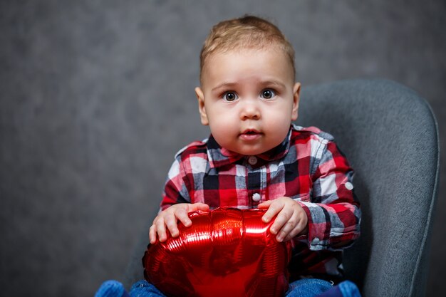 A little boy in a shirt plays with a balloon in the form of a heart