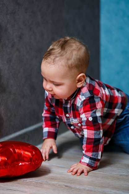 A little boy in a shirt plays with a balloon in the form of a heart