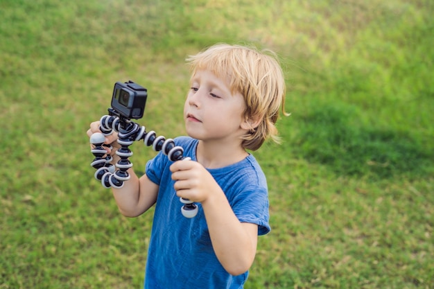 Photo little boy shoots a video on an action camera against a background of green grass