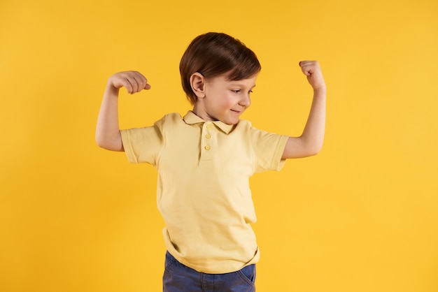 Little boy shows biceps isolated on yellow 