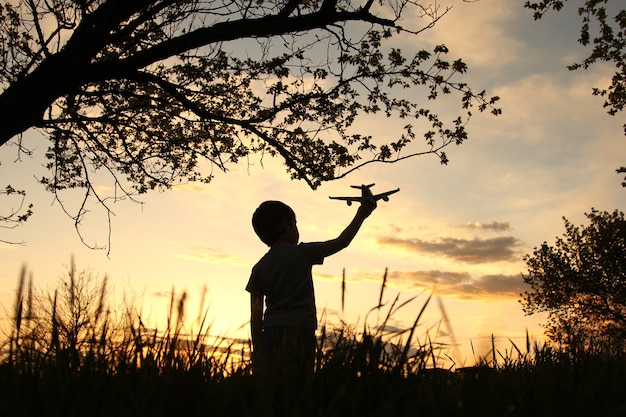 Photo a little boy in silhouette holding airplane in field at gorgeous sunset symbolizing peace in the world