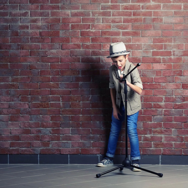 Little boy singing with microphone on a brick wall background