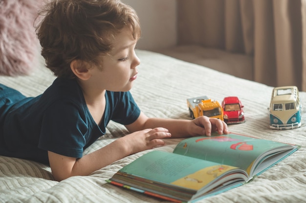 A little boy sits on a bed with a book