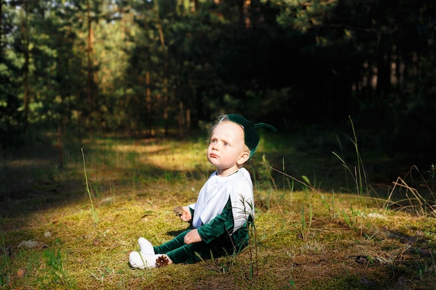 Little boy sits on a forest path in a snowdrop costume. boys dressed in a funny snowdrop costume with a hat