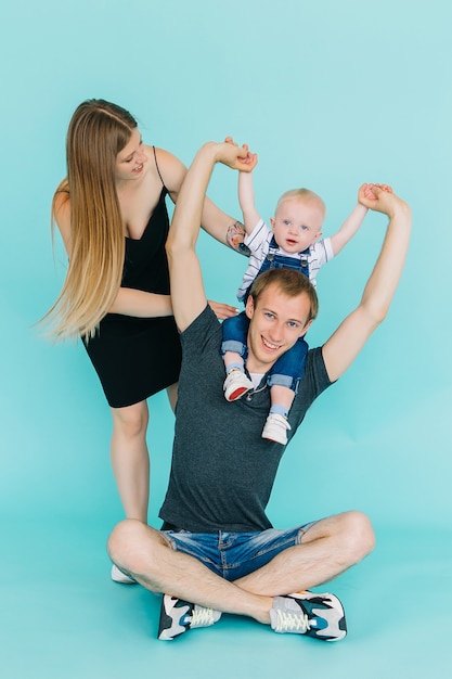 Foto il ragazzino si siede sul collo di suo padre isolato su blu, bella giovane madre stare vicino alla sua famiglia ..