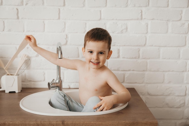 Little boy sits in the sink in the kitchen