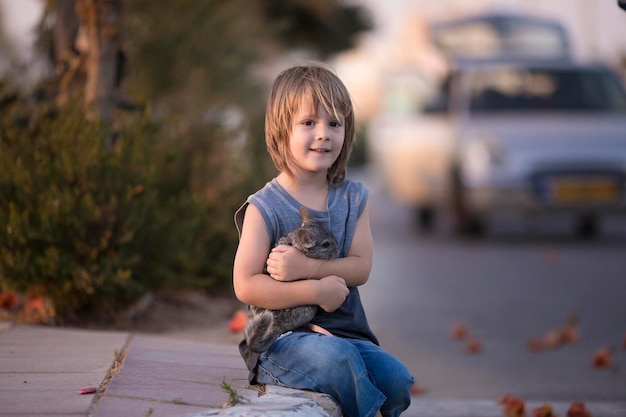 A little boy sits on the street and holds a chinilla in his hands