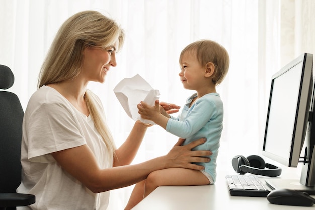 Little boy sitting on a desk distracting freelancer mother from paperwork