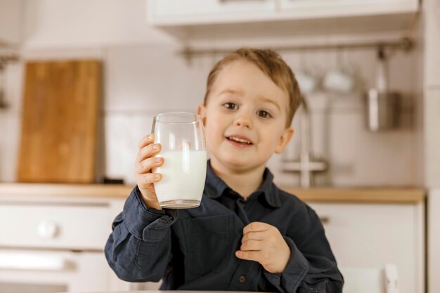 Little boy sitting in the kitchen and drinking milk. Fresh milk in glass, dairy healthy drink. Healthcare, source of calcium, lactose. Cosy and modern interior. Preschool child with casual clothing.