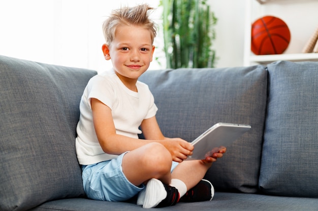 little boy sitting on sofa and using digital tablet at home