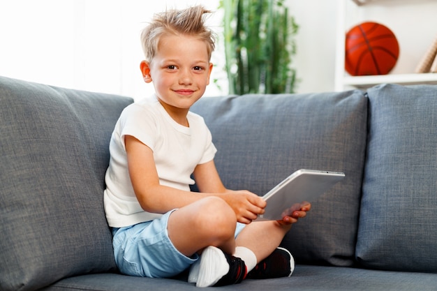 Little boy sitting on sofa and using digital tablet at home