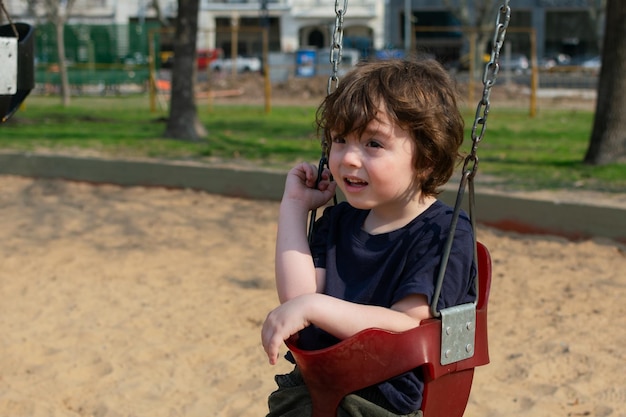 Photo a little boy sitting on the swing in the playground looking away