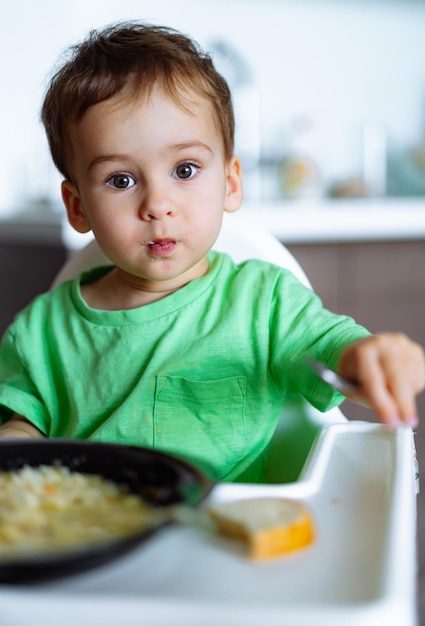 テーブル に 座っ て 食べ物 を 食べ て いる 小さな 男の子 料理 の 喜び を 発見 し て いる 好奇心 の ある 幼児