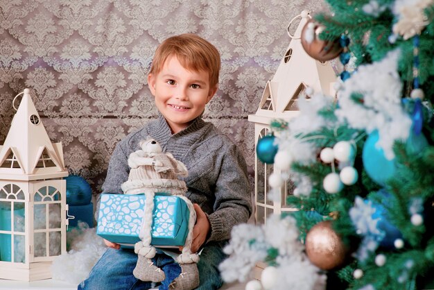 Ragazzino seduto con regalo di natale vicino all'albero di natale e decorazioni natalizie