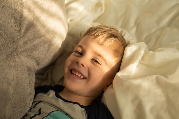 Little boy smiling lying on his back on the bed in the sun rays