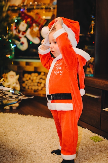 Little boy stand near Christmas tree with Santa Claus costume