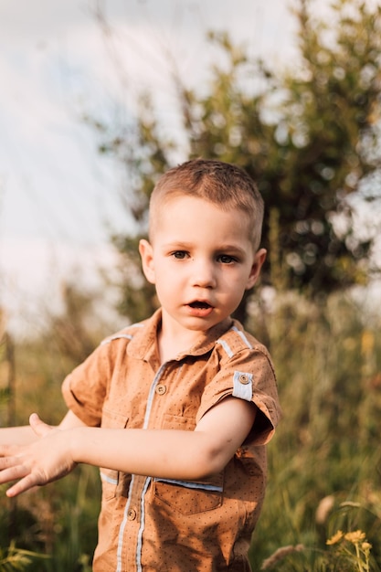 A little boy stands in nature and smiles