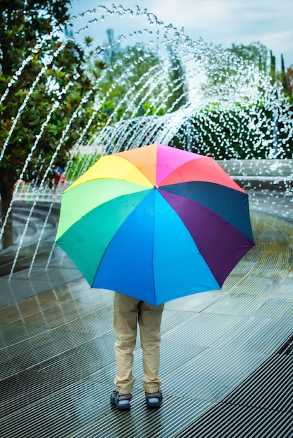 Little boy stands under an umbrella in a fountain