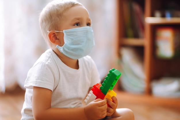 Little boy in sterile medical mask playing constructor at home