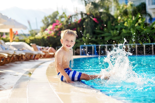 A little boy in striped shorts splashing feet in the pool next to the hotel