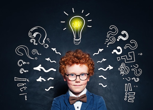 Photo little boy student in glasses with lightbulb on blackboard background brainstorming and idea concept