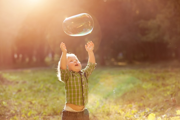 Photo little boy in the sunset catches soap bubbles