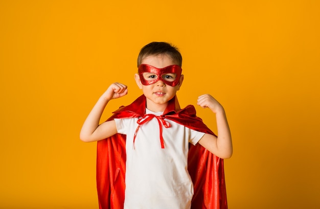 Little boy in a superhero costume shows power on a yellow surface with space for text