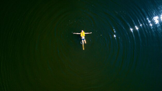 A little boy swims lying on his back in the middle of a river in the summer.