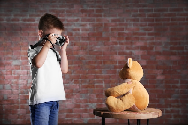 little boy taking photo of toy bear on brick wall