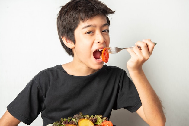 Little boy teenager eating tomato with salad for his meal