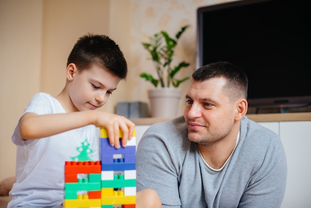 Маленький мальчик вместе с отцом играет конструктора и строит дом. Строительство семейного дома.