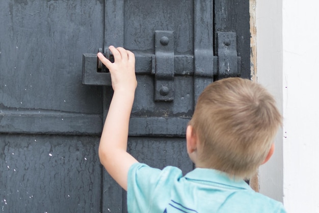 Маленький мальчик пытается открыть дверь Ребенок стоит перед запертой дверью