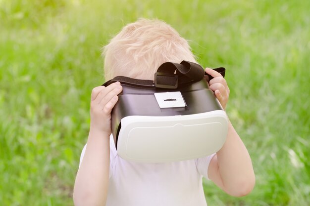 Little boy in a virtual reality helmet on a  of green grass