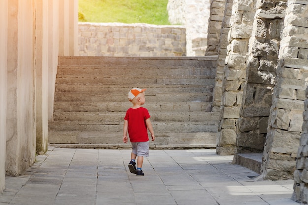 Little boy walking alone among the ancient walls, sunlight.