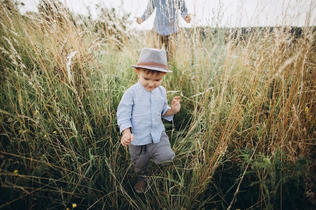 Little boy walking in meadow with high grass on sunset