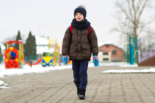 Little boy walking in the park. Child going for a walk after school with a school bag in winter. Children activity outdoors in fresh air. Healthy way of life concept.