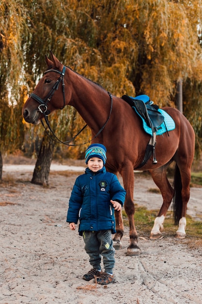 Little boy walking with horse in autumn park